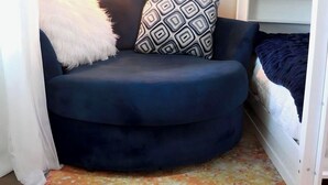 Ein Eckzimmer mit einem dunkelblauen Sofa, einem gemusterten Kissen, einer flauschigen weißen Decke, einem weißen Etagenbett und einem farbenfrohen Teppich.