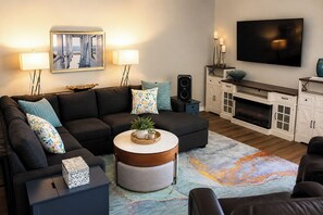 Un salon moderne avec un canapé d’angle, une table basse ronde, un téléviseur à écran plat et une cheminée.