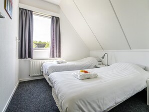 Ein kleines, sauberes Zimmer mit zwei Betten, einem Fenster mit Vorhängen, einer Heizung und einem Schreibtisch mit Lampe.