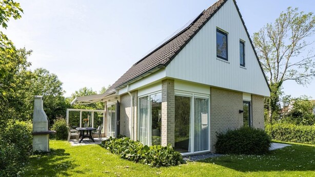Et moderne hus med skråt tag, store vinduer og en terrasse med udendørs møbler.
