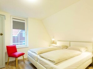 Ein Schlafzimmer mit einem Bett, einem Sessel, einem Nachttisch und einem Fenster.