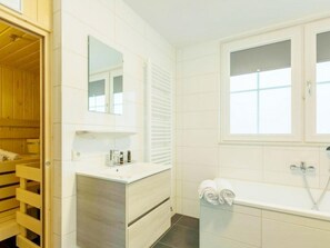Ein Badezimmer mit Duschkabine aus Holz, einem weißen Waschtisch mit Spiegel und einer Badewanne mit Handtüchern.