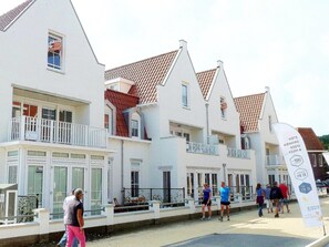 Eine Reihe weißer Gebäude mit roten Ziegeldächern, Balkonen und einer Flagge, die auf ein Radrennen hinweist.