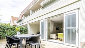 A patio with a table and chairs, a sliding glass door leading to a room, and a white brick exterior. - Apartment Near Koudekerke Beach (Koudekerke)
