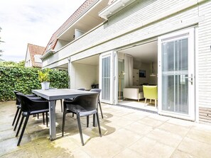 A patio with a table and chairs, a sliding glass door leading to a room, and a white brick exterior. - Apartment Near Koudekerke Beach (Koudekerke)