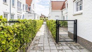 A narrow pathway flanked by white buildings with red-tiled roofs, leading to a gated entrance. - Apartment Near Koudekerke Beach (Koudekerke)