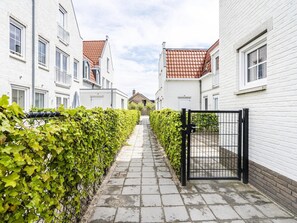 A narrow pathway flanked by white buildings with red-tiled roofs, leading to a gated entrance. - Apartment Near Koudekerke Beach (Koudekerke)