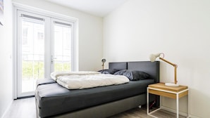 A bedroom with a bed, a bedside table with a lamp, and a view through a window. - Apartment Near Koudekerke Beach (Koudekerke)