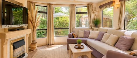 A living room with a fireplace, a television, a sofa, and large windows with curtains.