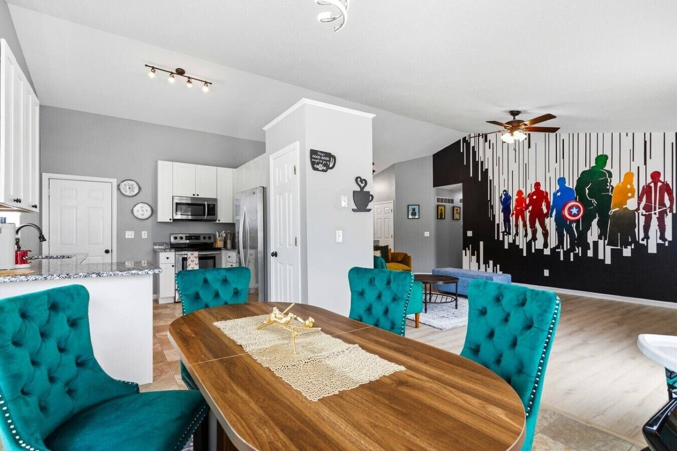 A modern kitchen with white cabinets, a central island, and teal upholstered chairs around a wooden dining table.