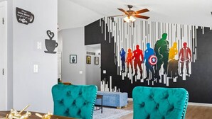 Una sala moderna con sillones tapizados en color verde azulado, una mesa de comedor de madera y un mural con vistas a la ciudad en la pared.
