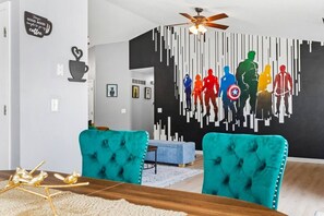 Ein modernes Wohnzimmer mit sesseln in petrolfarbenem Stoff, einem Holzesstisch und einer Stadtansicht als Wandgemälde.