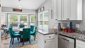 Una cocina con armarios blancos, encimera de granito y comedor con sillas color turquesa y una mesa.