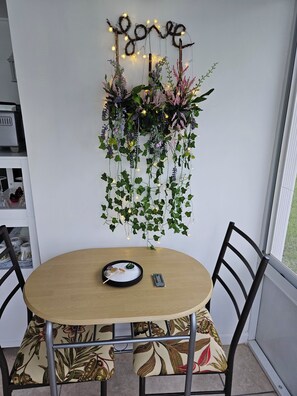 Un coin repas comprenant une table ronde, des chaises, un luminaire fixé au mur et une plante suspendue.