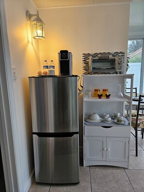 A kitchen with a stainless steel refrigerator, a microwave, a water dispenser, and a wall-mounted light fixture. - Cozy studio, independent entrance, with AC in vibrant Orlando neighborhood (Orlando)