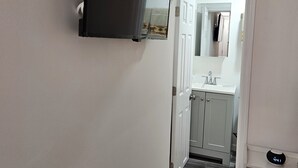A hallway with a door leading to a bathroom, a small table with a clock, and a wall-mounted shelf. - Cozy studio, independent entrance, with AC in vibrant Orlando neighborhood (Orlando)