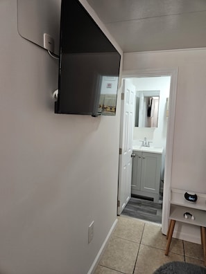 A hallway with a door leading to a bathroom, a small table with a clock, and a wall-mounted shelf. - Cozy studio, independent entrance, with AC in vibrant Orlando neighborhood (Orlando)