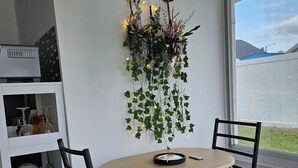 A dining area with a round table, two chairs, a wall-mounted clock, and a decorative hanging with lights and plants. - Cozy studio, independent entrance, with AC in vibrant Orlando neighborhood (Orlando)