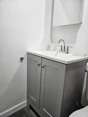 Une salle de bain avec un lavabo blanc, un miroir au-dessus et un meuble gris à deux portes.