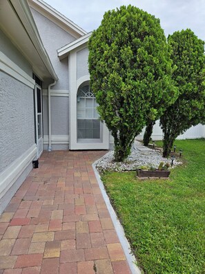 A house with a paved walkway, a small garden with shrubs, and a window with a metal grill. - Cozy studio, independent entrance, with AC in vibrant Orlando neighborhood (Orlando)