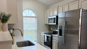 A modern kitchen with white cabinetry, stainless steel appliances, and a large island with a sink. - The Olive Mesa - HotTub - Fire pit - Sandbox (Lubbock)