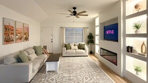 A modern living room with a sofa, a coffee table, a patterned rug, a fireplace, and a mounted TV. - The Olive Mesa - HotTub - Fire pit - Sandbox (Lubbock)