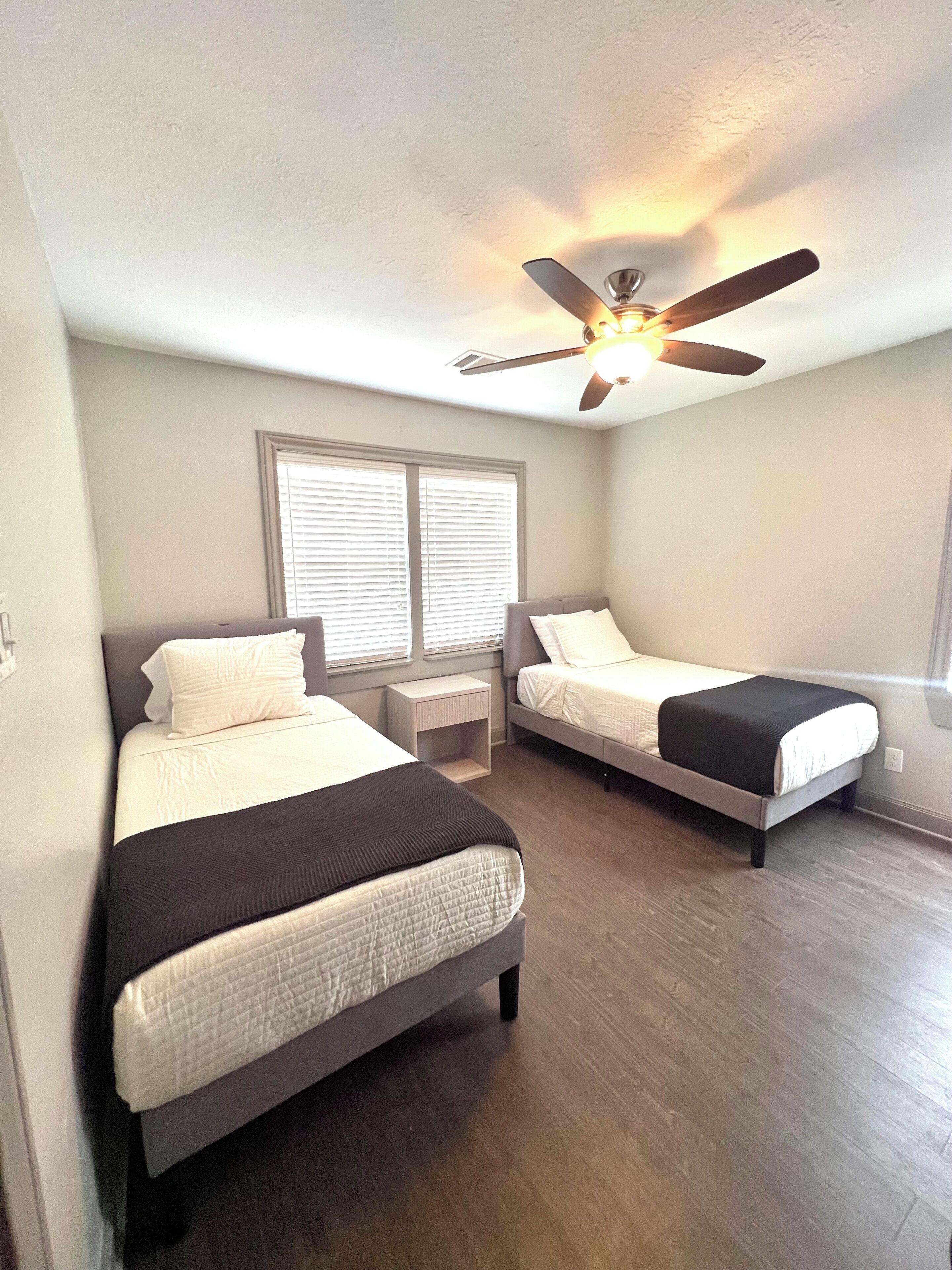A bedroom with two beds, a ceiling fan, and a window with blinds.