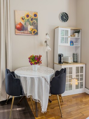 Un área de comedor con una mesa redonda, dos sillas, un jarrón de flores, un reloj y un armario blanco con estantes.