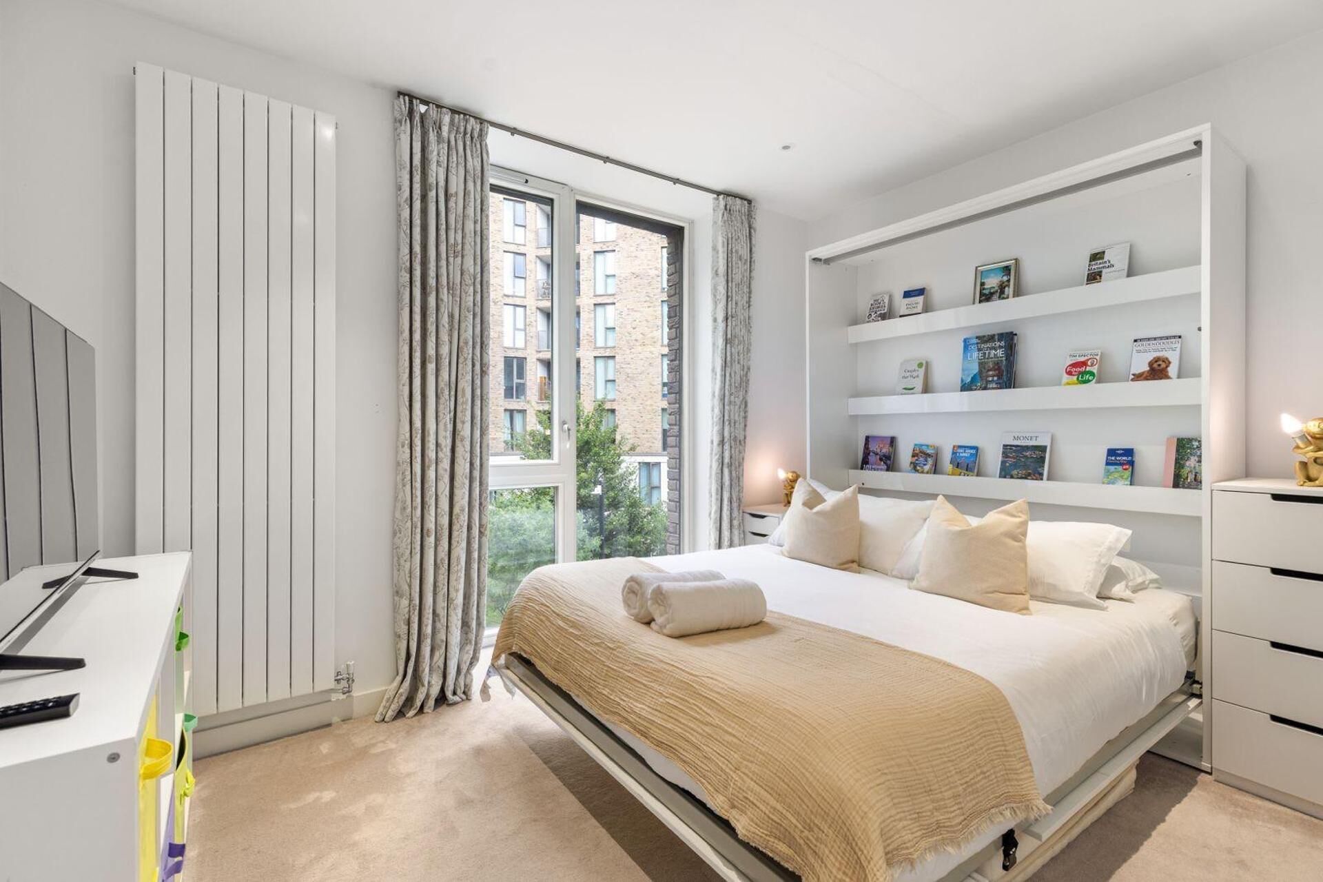 A modern bedroom with a bed, a desk, a bookshelf, and a window with curtains.