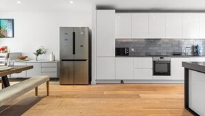 Eine moderne Küche mit weißen Schränken, einem Edelstahlkühlschrank, einer Mikrowelle und einem eingebauten Backofen.