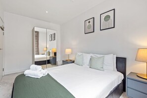 Ein Hotelzimmer mit einem Bett, zwei Nachttischen, einem Spiegel und zwei gerahmten Bildern an der Wand.
