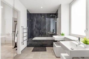 Ein modernes Badezimmer mit einer Duschkabine aus Glas, einer Badewanne und zwei Waschbecken.