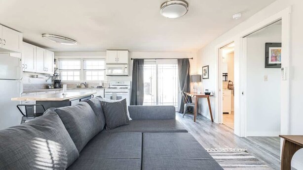 Un salon moderne avec un canapé gris, un coin repas et une cuisine dotée de meubles blancs.