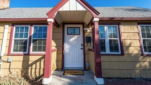Une maison avec une porte d’entrée, deux fenêtres de chaque côté et un petit porche.