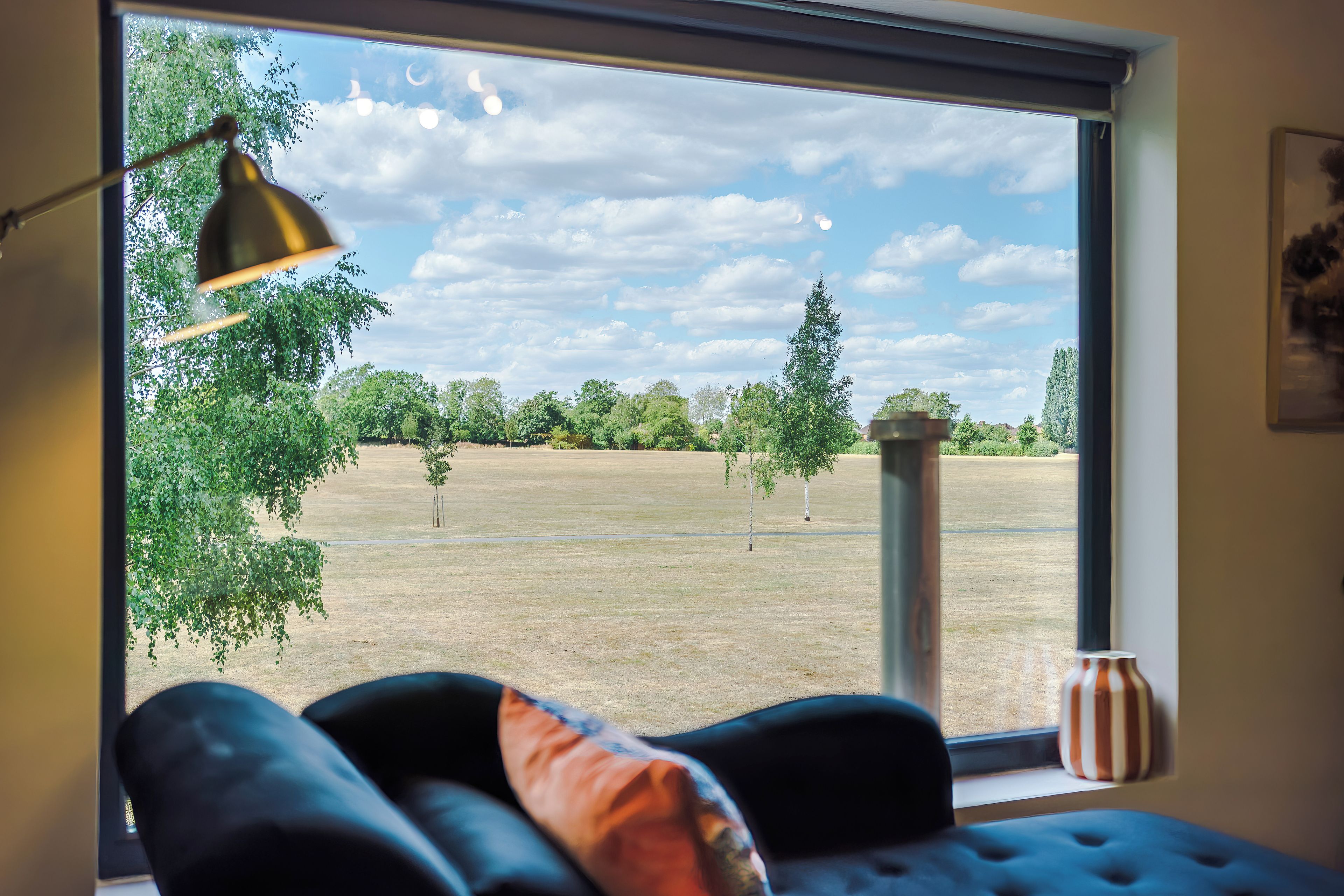 Ein Zimmer mit großem Fenster, einer schwarzen Couch, einer Lampe und einer Vase.