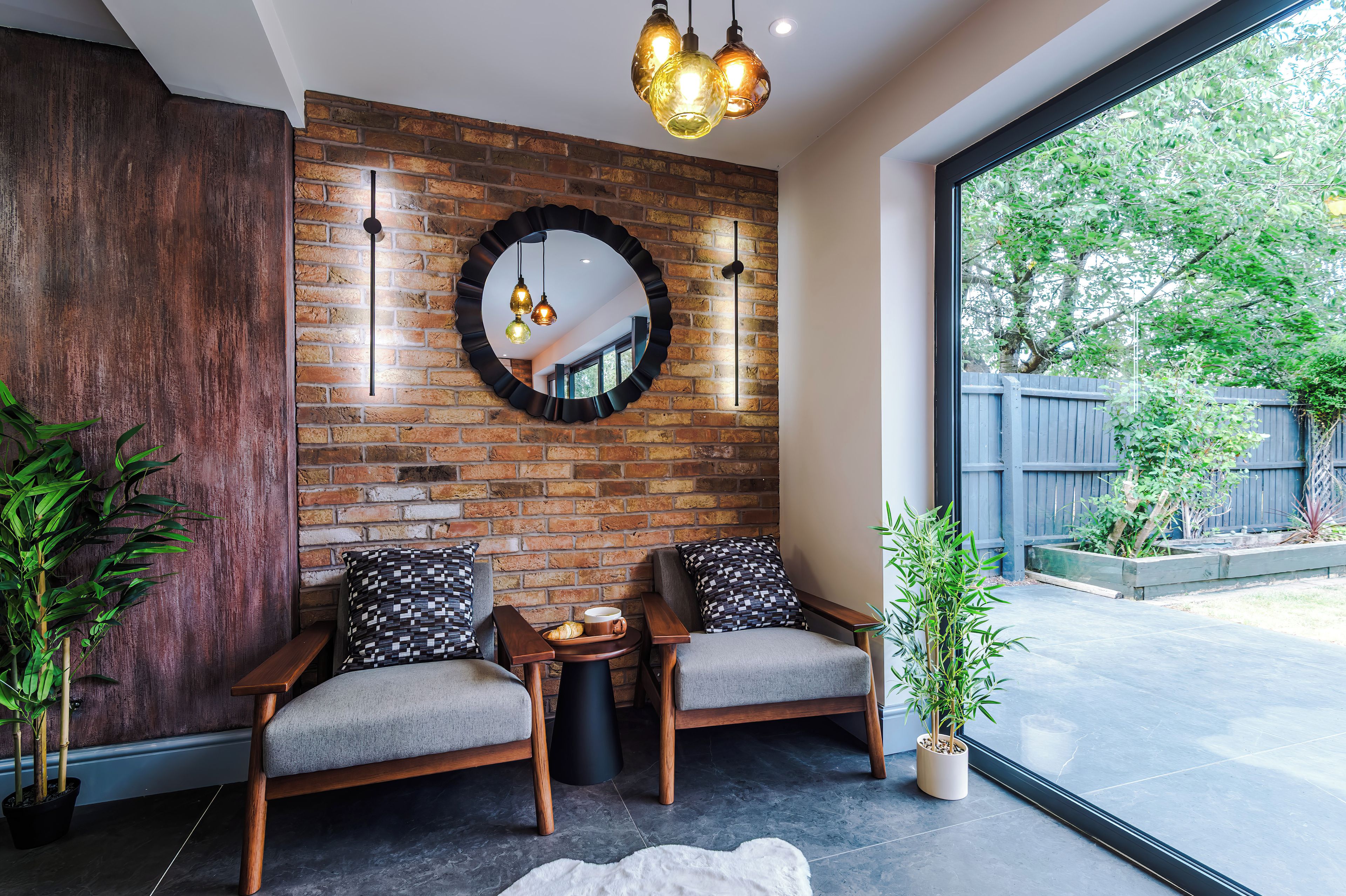 Ein modernes Interieur mit zwei Holzstühlen, einem runden Spiegel und einem kleinen Tisch mit einem Croissant.