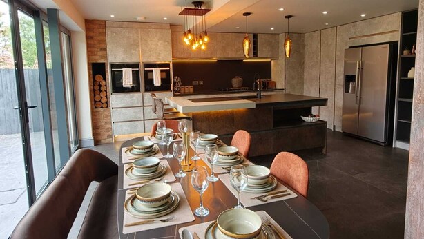Cozinha moderna com ilha central, mesa de jantar posta para seis pessoas e uma grande janela que proporciona iluminação natural.