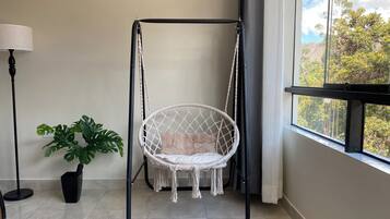 A room with a macrame hanging chair, a potted plant, a floor lamp, and a window with a view of trees.