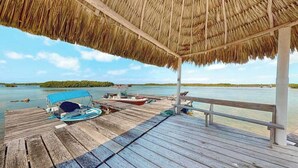 Une terrasse en bois surmontée d’un toit de chaume, un bateau et une vue sur une étendue d’eau calme.