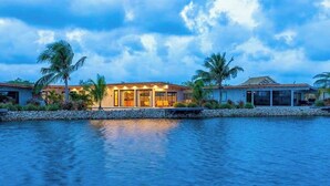 Une propriété située au bord de l’eau, avec une maison dotée de grandes fenêtres, d’une piscine et de palmiers.