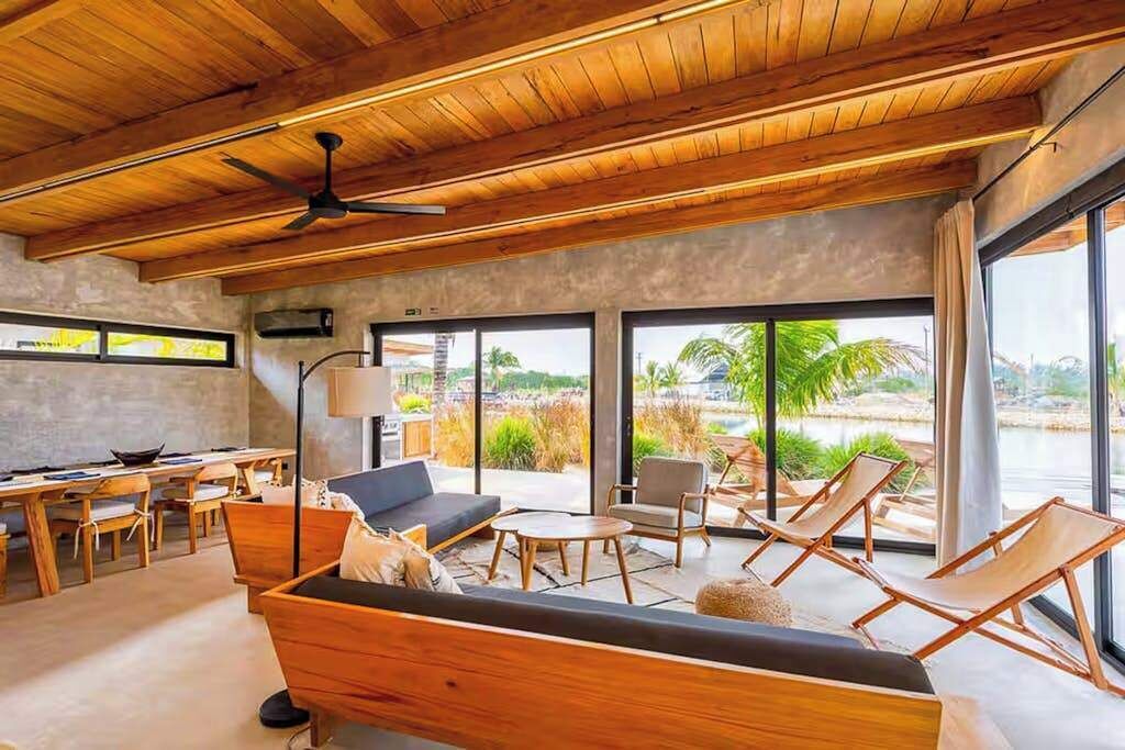 A modern interior with a wooden ceiling, large windows, a sofa, chairs, and a dining area.