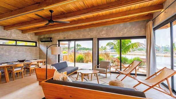 Un intérieur moderne avec un plafond en bois, de grandes fenêtres, un canapé, des fauteuils et un coin repas.