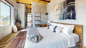 Een moderne hotelkamer met een houten plafond, een groot bed met witte lakens, een wandlamp en uitzicht op de omgeving.