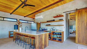 Une cuisine moderne dotée d’un îlot central, de tabourets de bar, d’étagères en bois et d’un ventilateur de plafond.