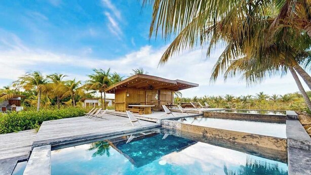 Un espace piscine doté d’une terrasse en bois, de chaises longues et d’un petit bâtiment.