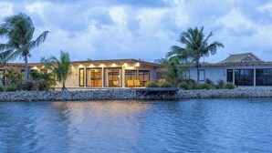 Un hôtel situé au bord de l’eau, doté d’une piscine, de palmiers et d’un éclairage extérieur soigné.
