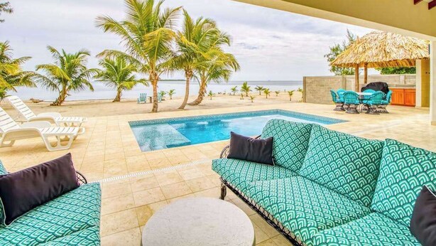 Un espace piscine aménagé avec des chaises longues, un canapé et un parasol en chaume.