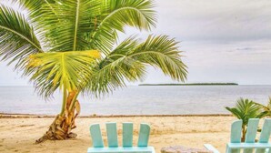 Une scène de plage avec deux chaises Adirondack bleu clair, une petite table et un grand palmier.