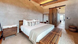 Une chambre à coucher comprenant un lit, une tête de lit en bois, des tables de chevet, un banc et un ventilateur de plafond.