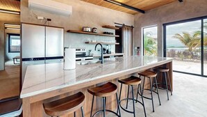 Une cuisine moderne avec un plan de travail en marbre, des tabourets en bois et une vue sur l’océan.
